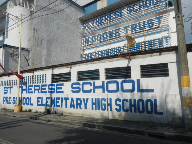 St. Therese-Schule in Manila, Philippinen, ein Gebäude mit Fenstern, einem Schild, einem Straßenpfahl, Bäumen, Drähten und einem bewölkten Himmel.