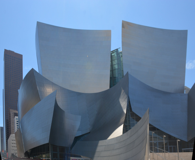 Modernes gläsernes Konzertgebäude in Los Angeles mit Treppen, Geländern und Menschen beim Eintreten; andere Gebäude und klarer blauer Himmel im Hintergrund.