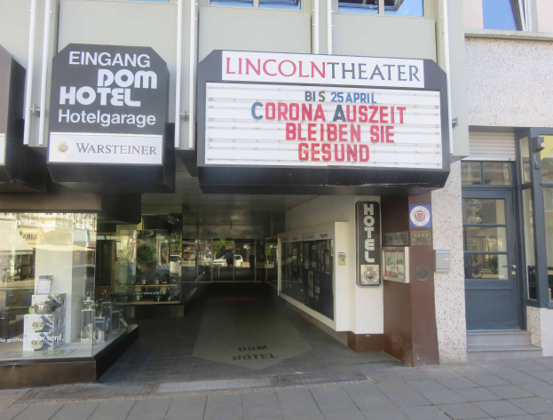 Das Lincoln Theater in Berlin, Deutschland, mit Glasfenstern und -türen und einer Texttafel draußen sowie einer belebten Stadtlandschaft im Inneren.