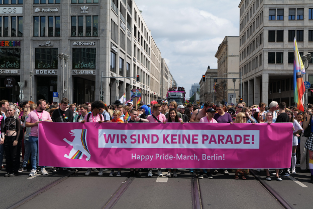 Eine Gruppe von Menschen marschiert mit einem pinken "Happy Pride March"-Schild die Straße in Berlin entlang.