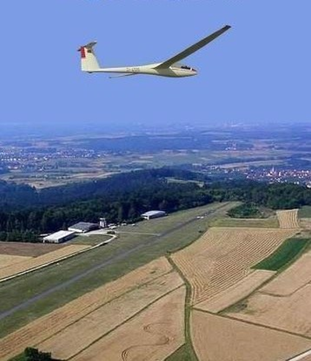 Ein Segelflugzeug fliegt über einem Feld mit Bäumen und Gebäuden im Hintergrund, mit Text oben auf dem Bild.