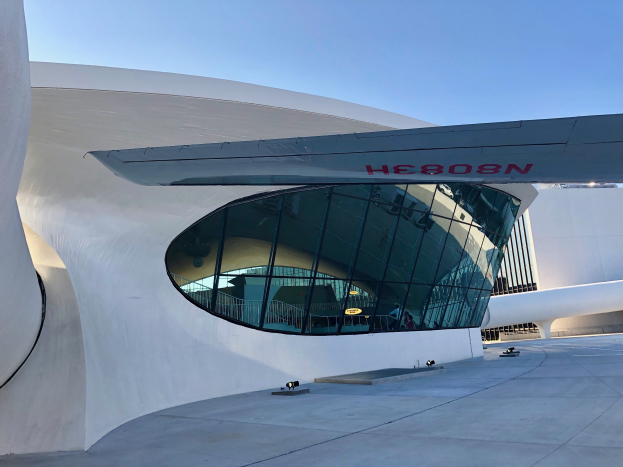 Ein großes weißes Gebäude mit gewölbtem Dach und einer großen Glaswand, beleuchtet von Lichtern, mit der Aufschrift "Museum of Contemporary Art, Los Angeles" darauf, unter einem klaren blauen Himmel.