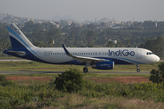 Indigo Airlines Airbus A320-200 auf dem Flughafen Mumbai mit Gras, Geb├Ąuden, Türmen, Bergen und Himmel im Hintergrund.