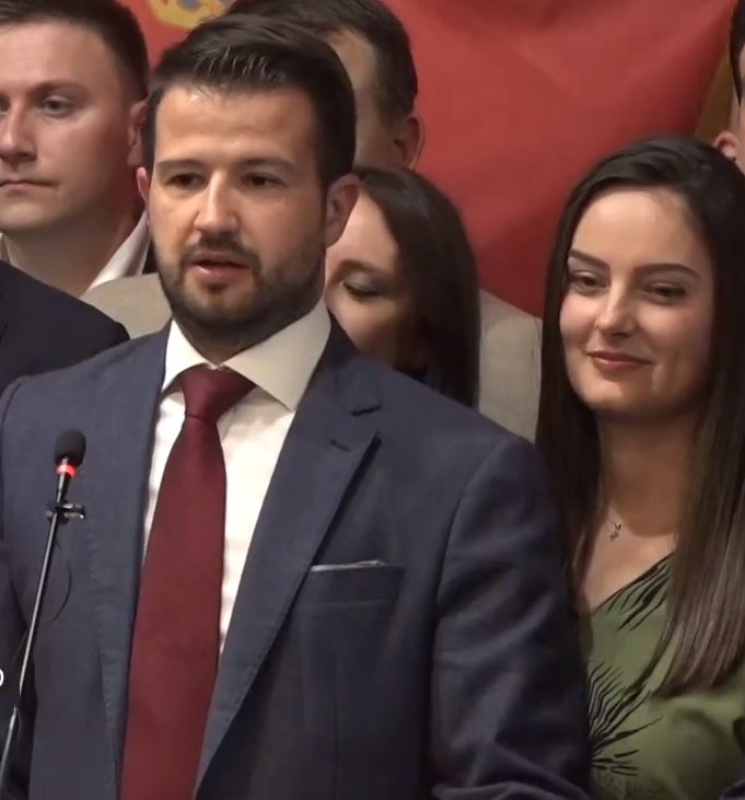 Ein Mann im Anzug spricht vor einem Publikum mit Mikrofon an einem Rednerpult, mit einem Banner im Hintergrund, wahrscheinlich zu einem sozialen Medienverbot der Regierung.