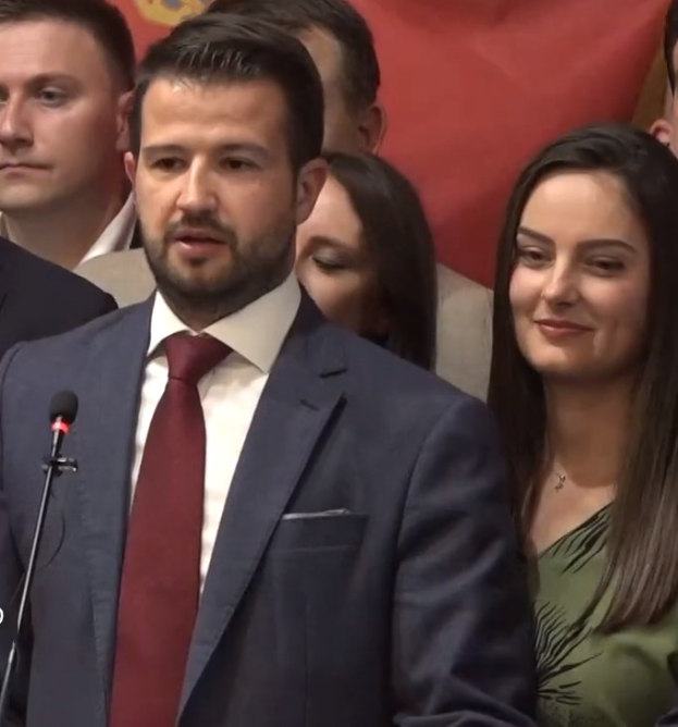 Ein Mann im Anzug spricht vor einem Publikum mit Mikrofon an einem Rednerpult, mit einem Banner im Hintergrund, wahrscheinlich zu einem sozialen Medienverbot der Regierung.