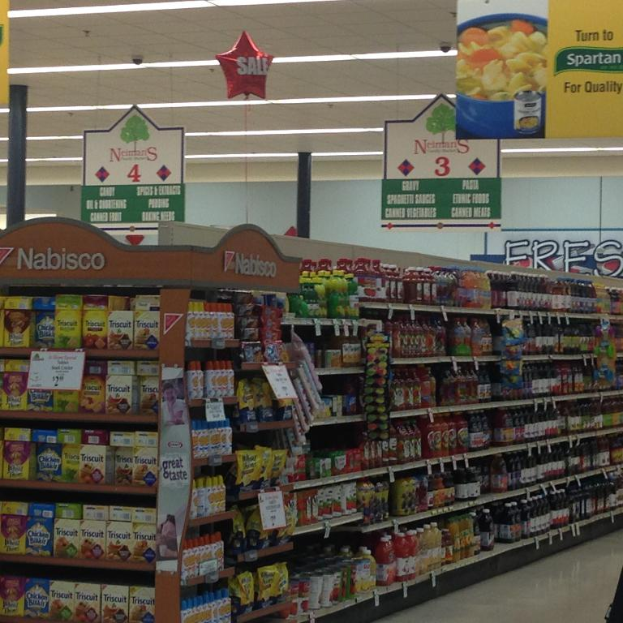 Ein Supermarkt-Innenraum mit Lebensmittelartikeln, Deckenleuchten und Schildern.