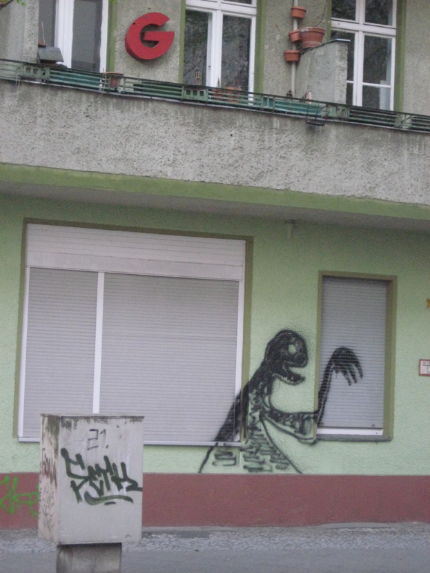 Ein Gebäude mit Fenstern und Graffiti, ein Brief an der Wand, eine kleine Säule und eine Straße im Vordergrund.