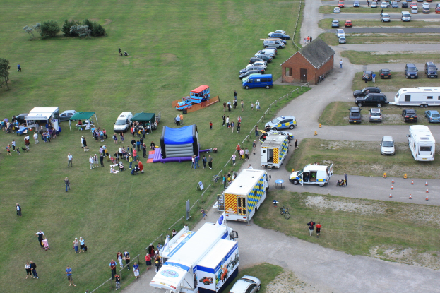 Eine Vogelperspektive auf eine Szene mit vielen parkenden Fahrzeugen, einigen Menschen in der Nähe von Zelten und einer Hütte in der Mitte.
