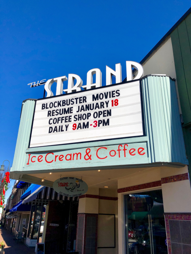 Der Strand-Blockbuster-Filme-Start am 18. Januar Kaffee-Shop-Gebäude mit einem Namensschild, einem Straßenschild, einer Gruppe von Bäumen, einigen Topfpflanzen und einem bewölkten Himmel.