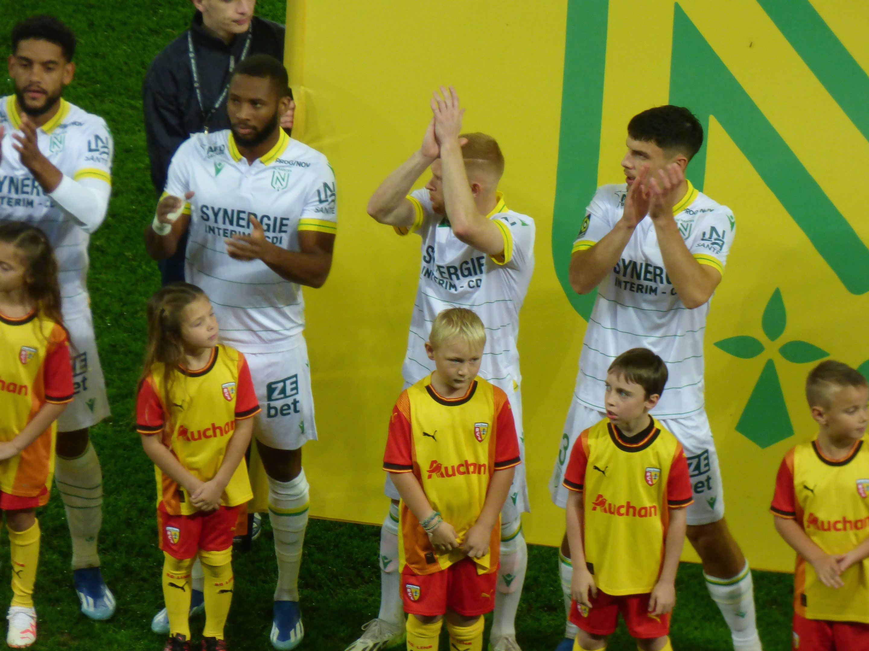 Eine Gruppe von Fußballspielern in Uniformen, die auf einem Ligue 1-Feld jubeln, mit einem "Ligue 1"-Schild im Hintergrund.