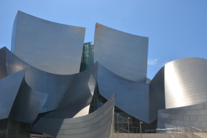 Die ARTIST Concert Hall in Los Angeles, ein modernes Gebäude mit Glaswänden und Treppen mit Geländern, die zum Eingang führen, umgeben von Laternenmasten, mit einer Tafel mit Text im Vordergrund und einem bewölkten Himmel im Hintergrund.