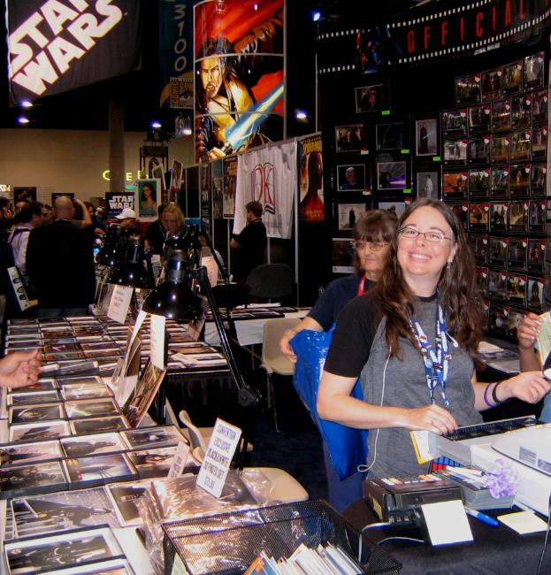 Eine Frau steht an der Kasse in einem belebten Laden, der mit Bildern, Büchern und aufgehängten Plakaten gefüllt ist, im Hintergrund kaufen Kunden ein.