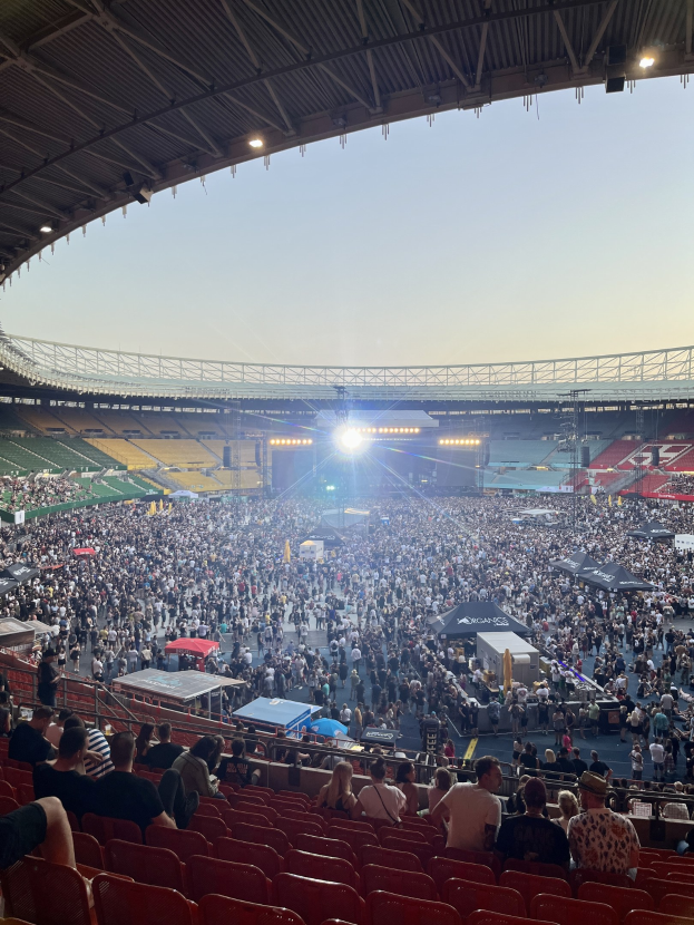 Großes Publikum in hell erleuchtetem Stadion mit Geländern, Wembley-Stadion in London im Hintergrund bei klarem Himmel.