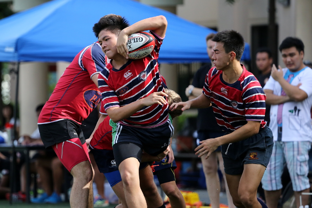 Eine Gruppe von Menschen, die draußen ein Spiel mit einem Jungen in der Mitte spielen, der einen Ball hält, während andere im Hintergrund stehen und zuschauen, neben einem blauen Zelt.