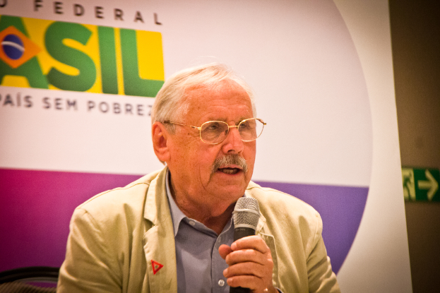 Eine Person, die in ein Mikrofon spricht und von einem Banner mit der Aufschrift 'Bundes' umgeben ist.