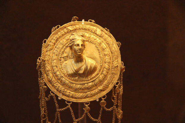 Goldene Medaille mit einer Frauengestalt, verziert mit feinen Details, vor einem dunklen Hintergrund.