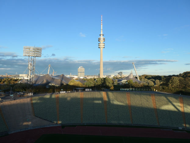Olympiastadion in Berlin mit dem Fernsehturm (Fernsehturm) im Hintergrund, umgeben von Bäumen, Gebäuden und Lichtern unter einem bewölkten Himmel.