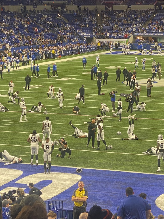 Ein Fußballspiel wird in einem Stadion mit Spielern auf dem Feld und Zuschauern im Hintergrund gespielt, einschließlich einer Person mit einer Kamera.