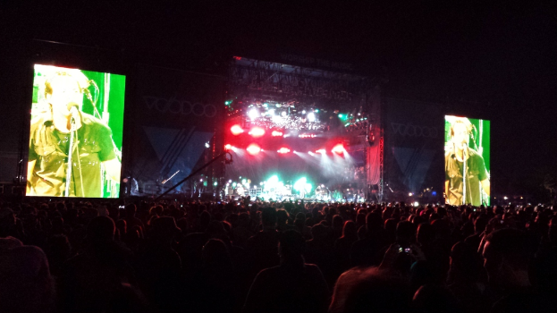 Eine Konzertszene mit einer Menge unten, ein großer Bildschirm links und ein weiterer rechts.