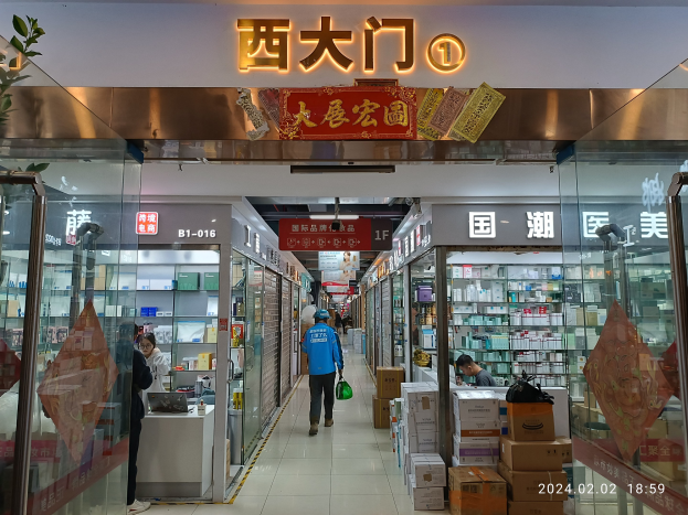 Innenansicht einer chinesischen Apotheke mit Glaswänden, einer Pflanze links, Regalen mit Artikeln, verstreuten Kartons und einer Namensschilder oben.