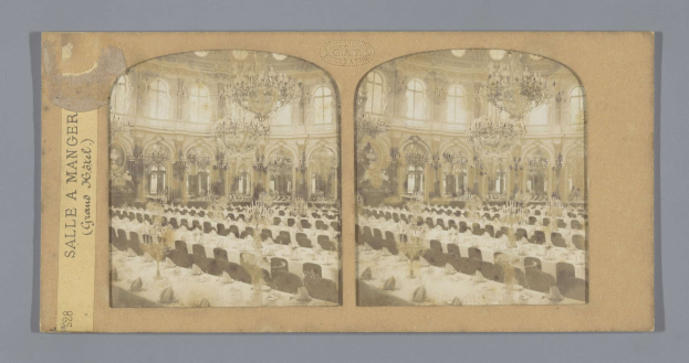Ein Schwarz-Weiß-Foto eines prunkvollen Hotel-Speisesaals mit langen Tischen, verzierten Kronleuchtern und hohen Fenstern, mit einer Tafel auf der linken Wand, die "Sale a Manger, Grand Hotel" lautet.