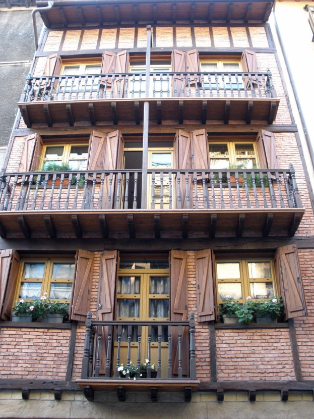 Ein mehrstöckiges Gebäude mit zahlreichen Fenstern, Balkonen, Geländern, Türen und Blumentöpfen mit Pflanzen in Straßburg, Frankreich.