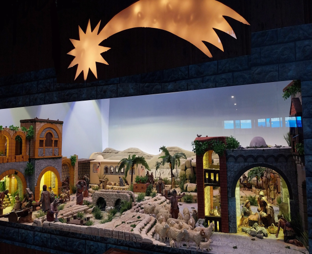 Eine Krippenausstellung im Museum mit Figuren, Tieren, Gebäuden und Grünpflanzen, beleuchtet von oben.