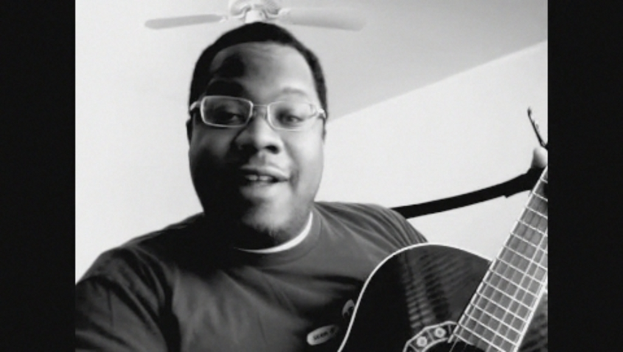 Ein Mann mit Brille spielt Gitarre, während ein Ventilator über ihm positioniert ist.