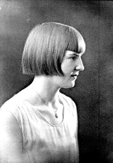 Ein Schwarz-Weiß-Foto einer Frau mit einem kurzen Bob-Haarschnitt, ihr Gesicht ist deutlich zu sehen, mit zur Seite schauenden Augen und leicht geöffneten Lippen.