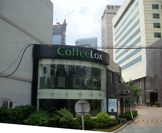 Ein Geschäftsgebäude mit ein paar Pflanzen davor, umgeben von vielen hohen Gebäuden und einigen Drähten.