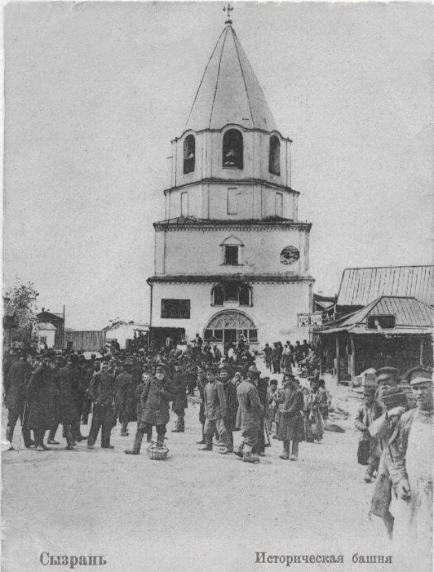 Schwarzes und weißes Foto einer Gruppe von Menschen, die vor der Kirche der Interzession am Nerl stehen, mit Häusern und Bäumen im Hintergrund.