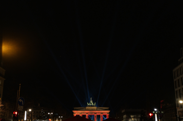 Das Brandenburger Tor in Berlin nachts, beleuchtet von Straßenlaternen, mit umliegenden Gebäuden, Bäumen, Pfählen, Verkehrszeichen, Schildern und Zelten gegen einen dunklen Himmel.