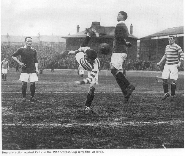 A group of men playing soccer on a field with spectators in the stands, buildings, and a clear sky in the background, with text at the bottom of the image.