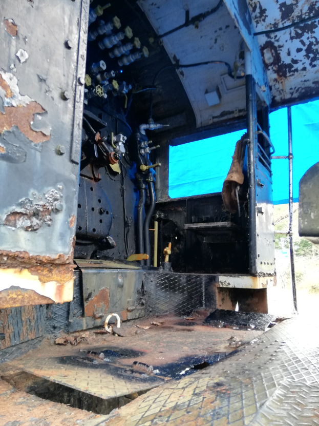 Das Innere eines verrosteten, baufälligen Lastwagens mit sichtbaren Gebrauchsspuren, vor einem Hintergrund aus Bäumen und einem klaren blauen Himmel.