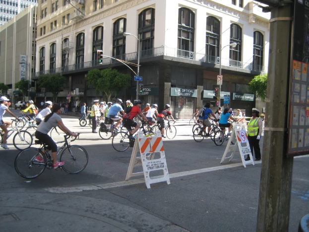 Mehrere Fahrradfahrer auf einer Straße mit einem Fahrzeug und einigen Bäumen im Hintergrund.