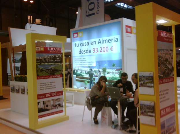 Eine Gruppe von Menschen, die um einen Tisch sitzen und auf einen Laptop schauen, mit mehreren Flyern, auf denen verschiedene Werbeanzeigen zu sehen sind.