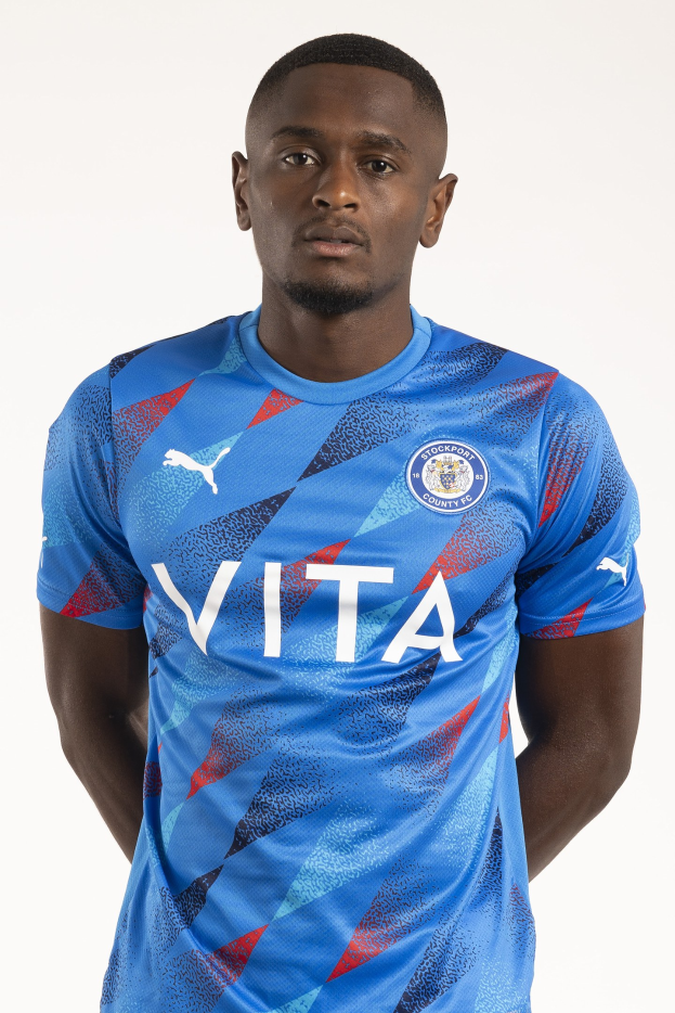 Ein Mann in einem blauen Leicester City Away-Shirt von der Saison 2018-19 steht mit Händen in den Taschen und einem leichten Lächeln.