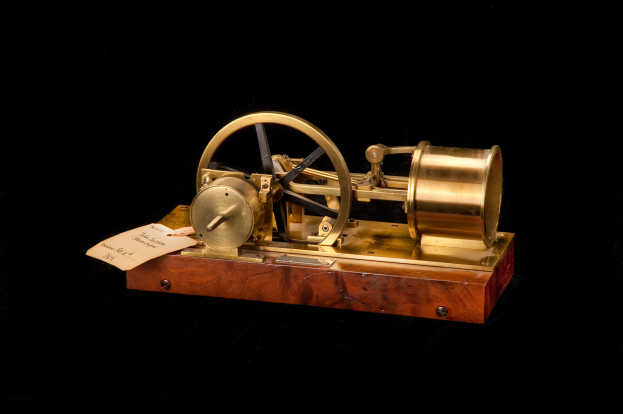 Altmodische Uhr mit einem Holzfuß, Metallrad und einem Papier-Zeitschalter, der an einem schwarzen Hintergrund angebracht ist.