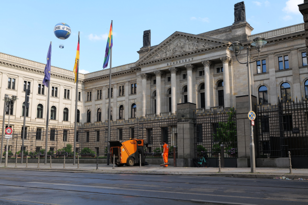 Großes modernes Gebäude mit vielen Fenstern, identifiziert als der Bundestag in Berlin, Deutschland, umgeben von Straßeninfrastruktur, Fußgängern und Flaggen, unter einem bewölkten Himmel.