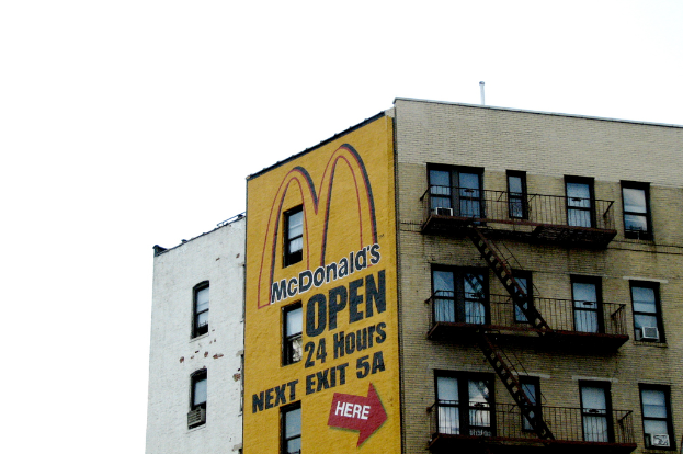 Ein Gebäude mit Text und einem Gemälde an seiner Wand, das Treppen, Geländer, Klimaanlagen an den Fenstern und ein Rohr an der Spitze mit dem Himmel zeigt.