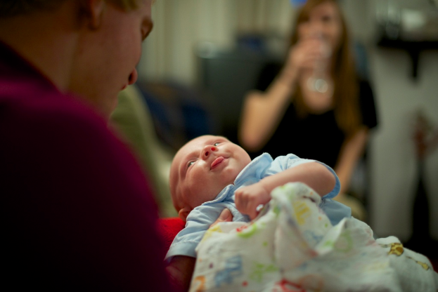Ein Mann hält ein Baby in seinen Händen, mit einer Frau vor ihm und einem unscharfen Hintergrund.