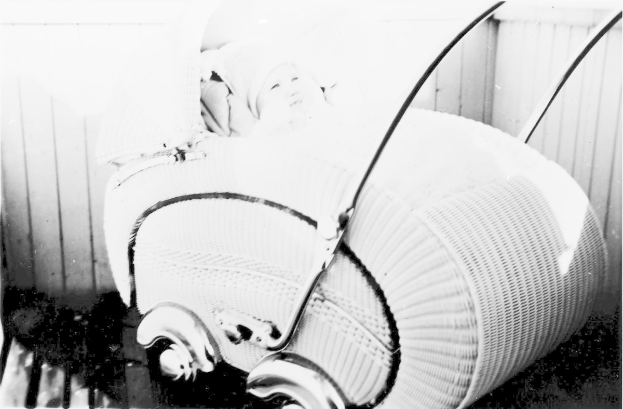 Ein Schwarz-Weiß-Foto eines Babys in einem Kinderwagen, das eine weiße Strampelanzug trägt und friedlich aussieht, mit einer Wand im Hintergrund.