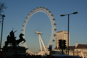 Gebäude und Masten rechts, ein großes Riesenrad in der Mitte und eine Skulptur links.