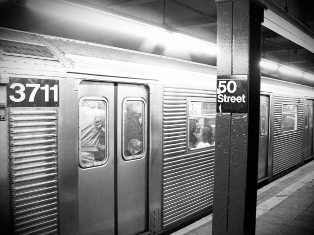 Ein Zug voller Menschen, mit einer Säule auf der rechten Seite, die ein Schild trägt, einem Bahnsteig unten und einem Dach oben.