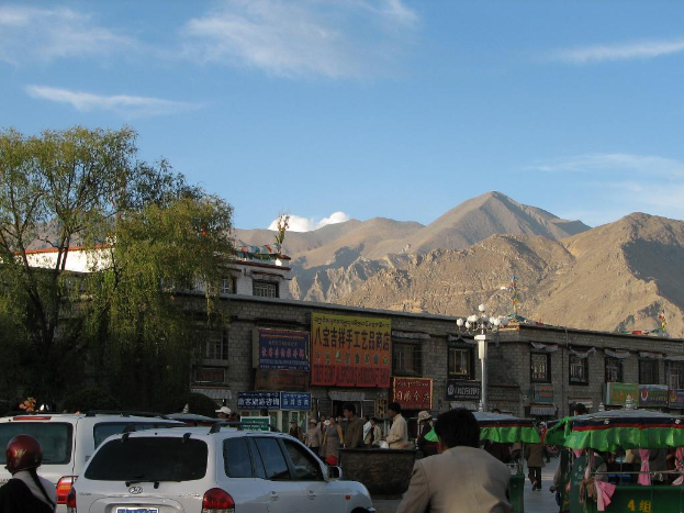 Eine Straßenszene mit Fahrzeugen, Menschen, Zelten, Polen, umgeben von Bäumen, Gebäuden und Bergen im Hintergrund.
