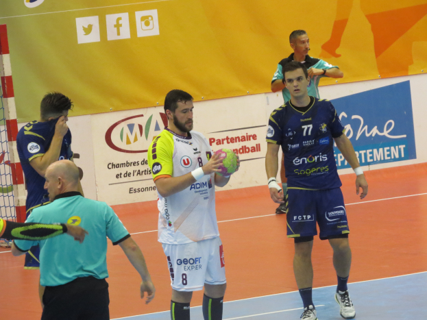 Eine Gruppe von Männern steht auf einem Futsal-Platz, einer hält einen Ball, daneben ein Tor und im Hintergrund Banner.