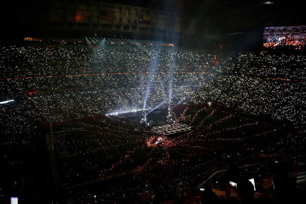 Große Menschenmenge in einem hell erleuchteten Stadion bei Nacht mit einem Bildschirm, der rechts die Ergebnisse der Super Bowl XLVII-Halbzeitshow anzeigt.