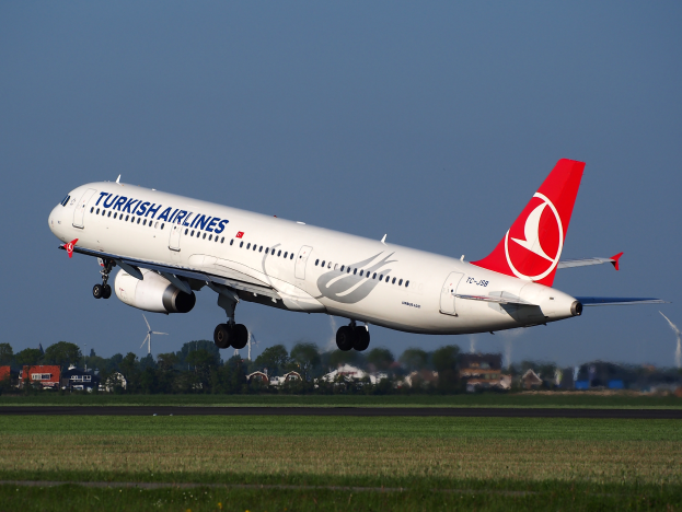 Ein Airbus A330-300 der Turkish Airlines startet vom Frankfurter Flughafen, mit Gras, Gebäuden, Bäumen und Windmühlen darunter unter einem klaren blauen Himmel.