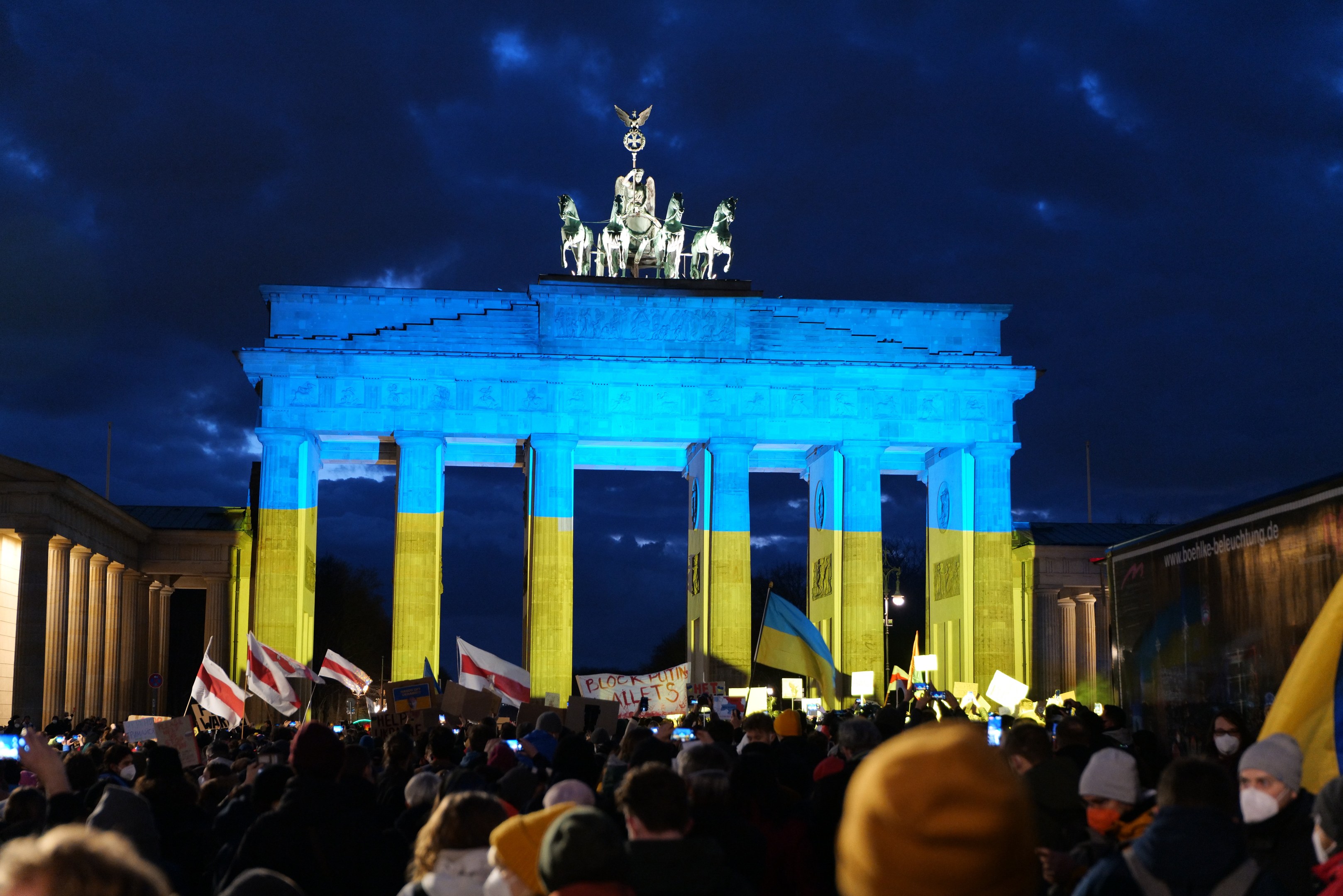 Eine Menschenmenge steht vor dem Brandenburgertor in Berlin, Deutschland, mit Fahnen und Schildern und einem Banner auf der rechten Seite des Bildes.