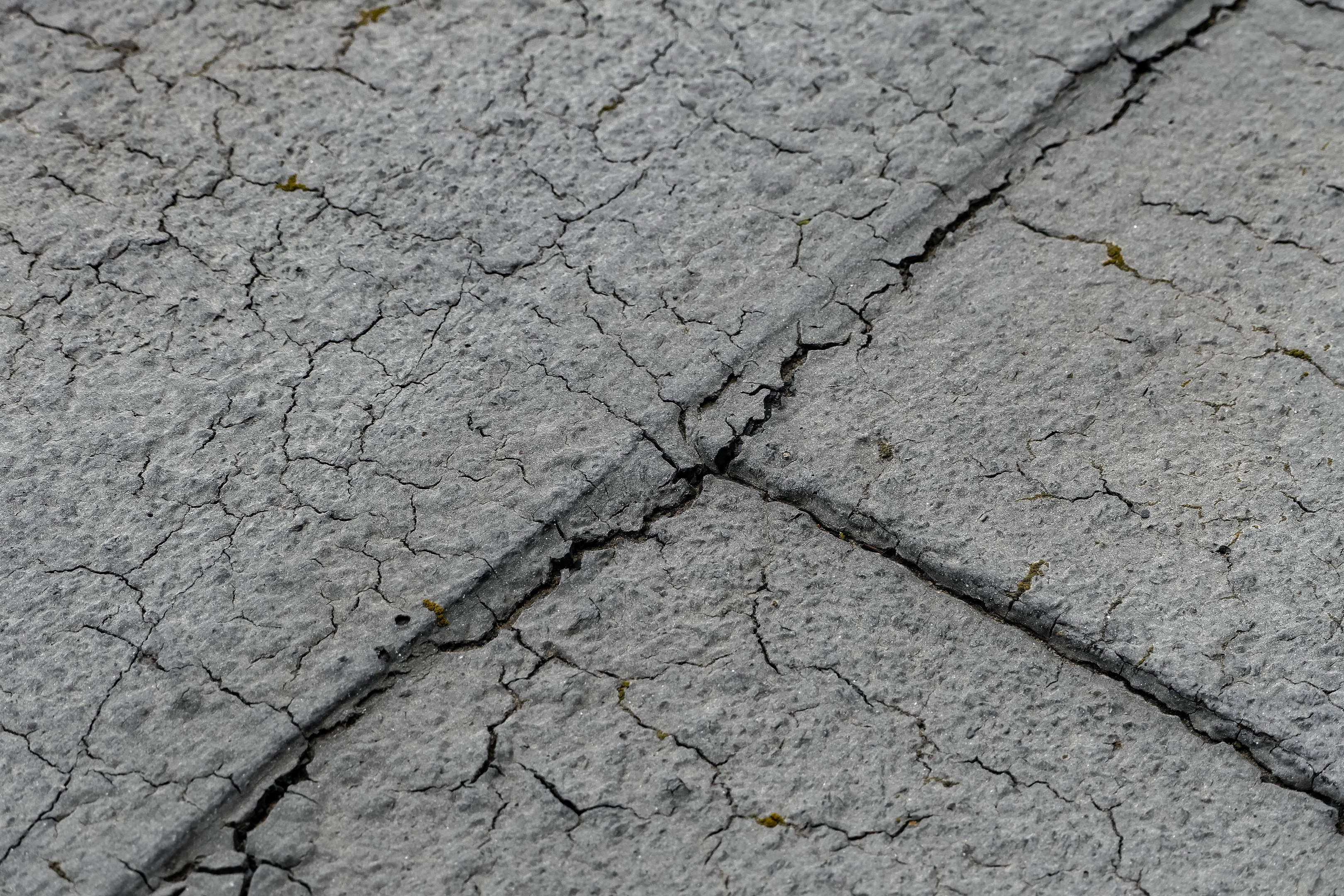 Nahaufnahme einer gebrochenen und verwitterten Straßenoberfläche mit tiefen, breiten Rissen und einer unebenen, rauen Textur.